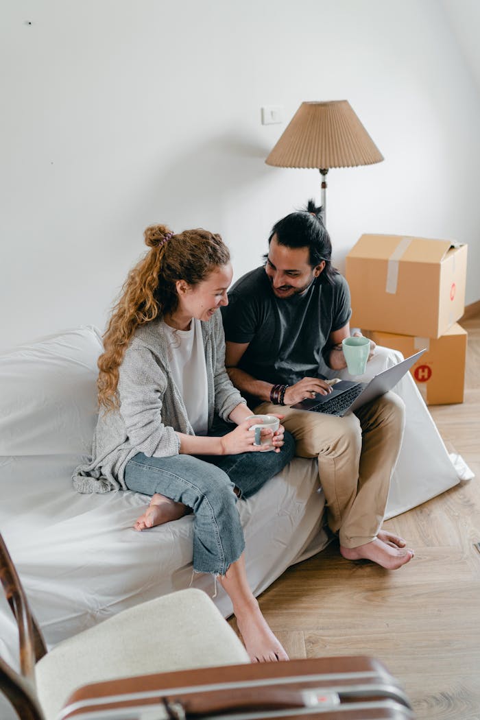 gallery-01 Joyful couple using a laptop and coffee in their new apartment, surrounded by moving boxes.